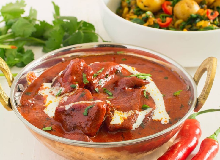 Curry served in a metal bowl with coriander and chillies next to the bowl